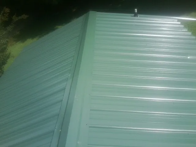 New green metal panels meeting at the ridge of a roof — Flat Roof Repair work by our crew in Hinton