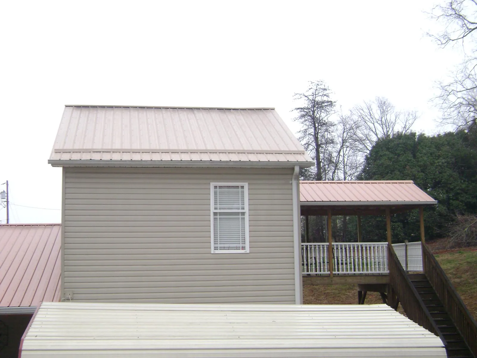 Tan metal roofs on a two story addition and attached porch, from a Roof Replacement job in Hinton